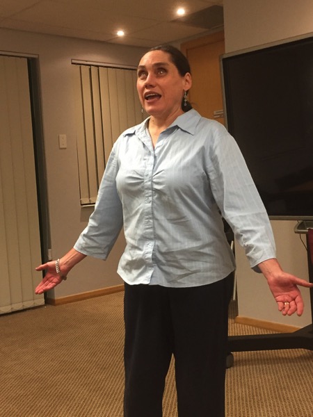 The image shows Lois speaking in front of an audience
