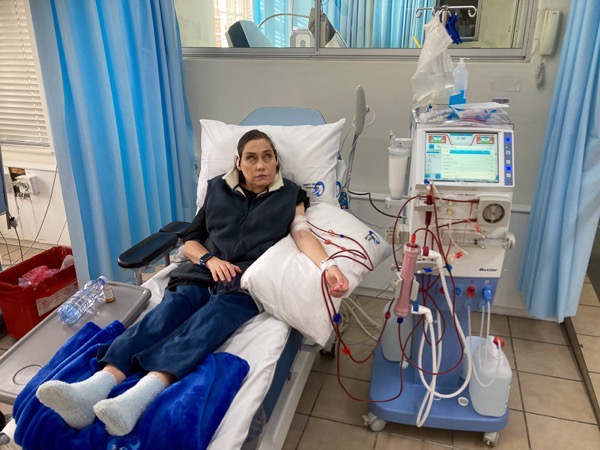 Alt text: A woman with shoulder length dark hair lies on a medical bed beside a dialysis machine