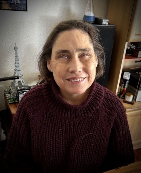 lois 1.jpg A woman with short dark brown hair framing her face. She is wearing a deep maroon knitted jersey with a high collar loosely around her neck.